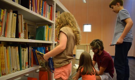 Foto del rincón infantil de la biblioteca de la FIC con dos niñas, un niño y un adulto buscando y leyendo libros.