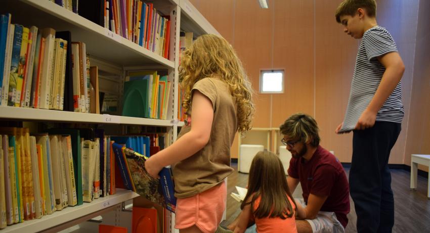 Foto del rincón infantil de la biblioteca de la FIC con dos niñas, un niño y un adulto buscando y leyendo libros.
