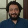 Primer plano, hombre, de pelo oscuro con rulos y barba, viste camisa azul. 