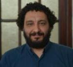 Primer plano, hombre, de pelo oscuro con rulos y barba, viste camisa azul. 