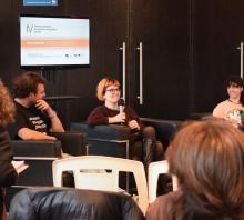 Fotografía de la mesa temática de cierre, protagonizada por tres estudiantes, dos mujeres y un varon. Una de las jóvenes, de pelo naranja y buzo marrón, habla al auditorio. 